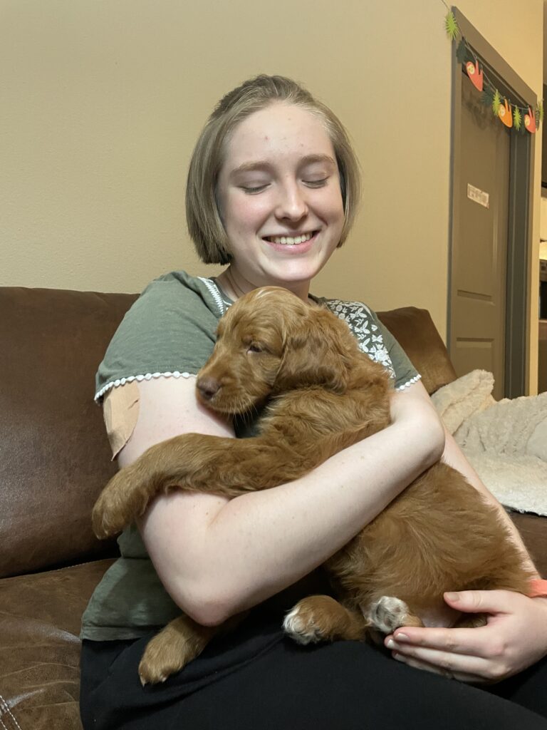 Clara, a young white woman with short blond hair, cradling a golden doodle puppy.